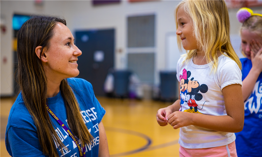 A woman with brown hair talks to a young student with blonde hair